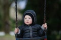 Sad, worried little boy swinging by himself, left alone unattended, looking for parents