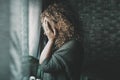 Sad and worried woman side portrait at home in the dark looking outside the window. Worried and lonely female alone indoor. Royalty Free Stock Photo