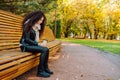 Sad young afro-haired woman sit alone on a wooden bench in autumn park at sunny warm day. Portrait of alone woman Royalty Free Stock Photo