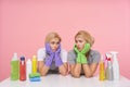 Sad young blonde cleaning ladies in rubber glove leaning their heands on raised hands and looking drearily on each other, sitting