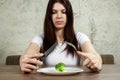 Sad young brunette woman dealing with anorexia nervosa or bulimia having small green vegetable on plate. Dieting problems, eating