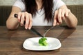 Sad young brunette woman dealing with anorexia nervosa or bulimia having small green vegetable on plate. Dieting problems, eating