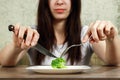 Sad young brunette woman dealing with anorexia nervosa or bulimia having small green vegetable on plate. Dieting problems, eating