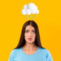 Sad young european female with abstract cloud and rain sign above head  on yellow studio background Royalty Free Stock Photo