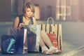 Sad young fashion woman with shopping bags sitting on city sidewalk Royalty Free Stock Photo