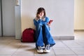 Sad young female student with backpack smartphone sitting on the floor Royalty Free Stock Photo