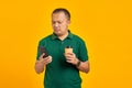 Sad young handsome man holding smartphone and cup of coffee on yellow background Royalty Free Stock Photo