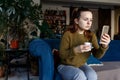 Sad young lonely woman in depression looking at phone gets bad news  sitting on sofa  drinking coffe.depressed female receiving Royalty Free Stock Photo