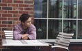 Sad young man sitting at a table near a wall Royalty Free Stock Photo