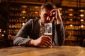 Sad young man in a suit looking at a glass of beer while sitting at a table in a pub. A man drinks after work in a pub. Royalty Free Stock Photo