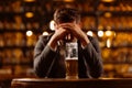 Sad young man in a suit looking at a glass of beer while sitting at a table in a pub. A man drinks after work in a pub. Royalty Free Stock Photo