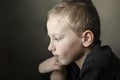 Sad young pre-school boy looking down and thinking. Unhappy child with sad face on dark background Royalty Free Stock Photo