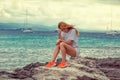 Sad young serious woman sitting on the rock looking down with sea ocean sky background Royalty Free Stock Photo