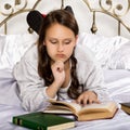 Sad young student girl reads a book while lying on a bed doing homework Royalty Free Stock Photo