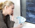 Sad young woman counts money for window repair with the burst, broken glass