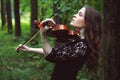 Sad young woman enthusiastically playing the violin romantic work in the Park among the trees