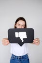 Sad young woman holding Dislike button icon of social media