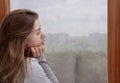 Sad young woman looking out window, lost in thought, copy space. Seasonal depression concept Royalty Free Stock Photo