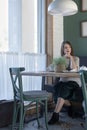 Sad young woman sitting in cafe alone with white cup of tea coffee latte and wait someone. Vertical frame Royalty Free Stock Photo