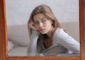 Sad young woman sitting at home and looking out window at falling rain, suffering from autumn depression