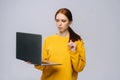 Sad young woman student holding laptop computer and typing on isolated gray background. Royalty Free Stock Photo