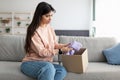 Sad young woman unpacking wrong parcel, delivery mistake