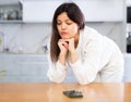 Sad young woman waiting for phone call in home kitchen