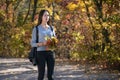 Sad young woman is walking along the alley of the autumn park. Young lonely girl with bouquet leaves in the forest