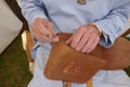 Saddler. Leather craftsman at work. He sews a bag by hand. Close-up.