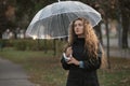 Sadness attractive woman with long hair in autumn park in rainy weather under transparent umbrella. Portrait of beautiful girl Royalty Free Stock Photo