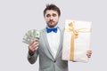 Sadness young bearded man in gray suit and blue bow tie standing and thinking that dont want to spend lot af dollars for big gift