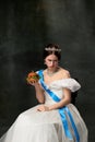 Sadness. Young beautiful woman in image of queen or princess in white medieval outfit holding big burger on dark