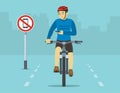 Safe bicycle riding. `No phones` sign on a city road. Front view of a cyclist looking at phone while cycling.