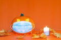 Safe Halloween 2020 during Covid-19 pandemc. Halloween carved luminous pumpkin,candle with face mask orange wall