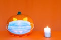 Safe Halloween 2020 during Covid-19 pandemc. Halloween carved luminous pumpkin,candle with face mask orange wall