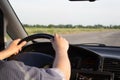 Safe journey concept. Both hands of man keep hold on steering wheel while driving a car on a country road