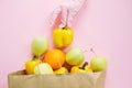 Safe shopping in quarantine. Hand in pink glove putting yellow pepper in paper bag with groceries on pink background flat lay.