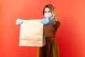 Safe shopping on quarantine. Woman in protective mask and gloves giving paper bag, food purchase Royalty Free Stock Photo