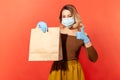 Safe shopping on self-isolation. Woman in protective mask and gloves holding paper bag and showing thumbs up Royalty Free Stock Photo