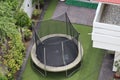 A safe trampoline is kept in the green garden. Kids like to jump on elastic circular rubber kept at home.