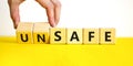 Safe or unsafe symbol. Concept word Safe Unsafe on wooden cubes. Businessman hand. Beautiful yellow table white background.