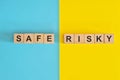 Safe versus risky in investment and business concept. Wooden blocks typography in blue and yellow background. Royalty Free Stock Photo