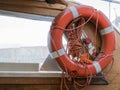 Safe water support aid circle with rope. Rescue red life buoy on wooden background of ship or boat. Royalty Free Stock Photo