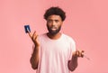Confused black man holding credit card and cellphone