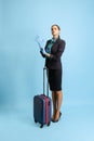 Studio shot of beautiful young girl, flight attendant in uniform with suitcase isolated on blue studio background.