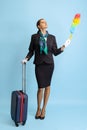 Studio shot of beautiful young girl, flight attendant in uniform with suitcase isolated on blue studio background.