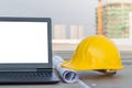 The safety helmet and the blueprint with laptop has white screen isolated at construction site with crane background Royalty Free Stock Photo