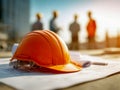 Safety helmet placed on architectural blueprints with construction workers discussing project in blurred background at sunset on Royalty Free Stock Photo