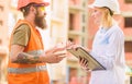 Safety inspector concept. Woman inspector and bearded brutal builder discuss construction progress. Construction site Royalty Free Stock Photo