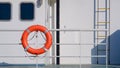 Safety orange lifebuoy hanging on steel guardrail on deck of the white ship
